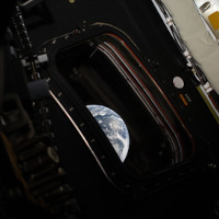 Part of the Earth's disk seen through the deep frame of an Orion spacecraft window against the dark interior